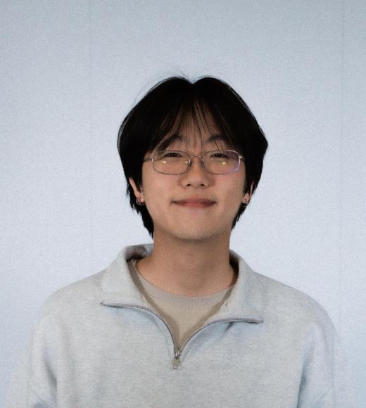 Studio photo: smiling young person with glasses and dark hair wearing gray pullover