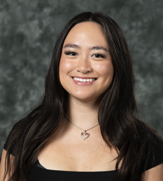 A girl wearing a black shirt is smiling in front of a gray backdrop.