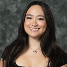A girl wearing a black shirt is smiling in front of a gray backdrop.
